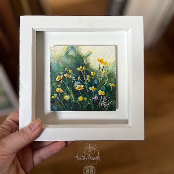 Framed miniature painting of golden buttercups in a meadow with dapples of sunlight on a dark green teal background