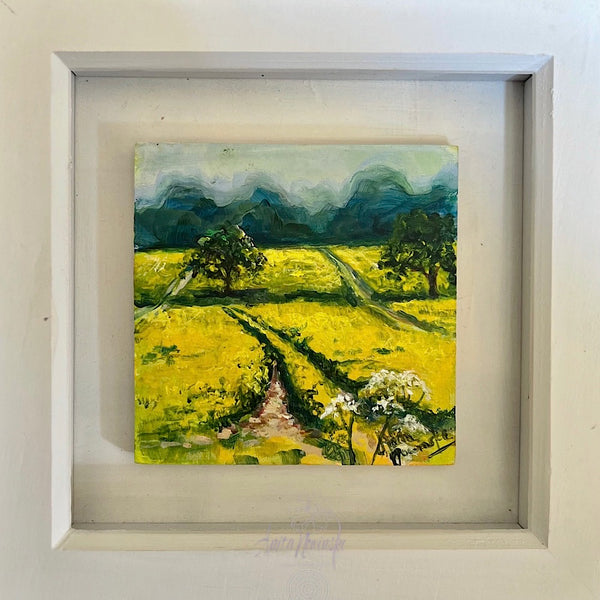 Framed painting of a landscape with a yellow rapeseed field and green trees.