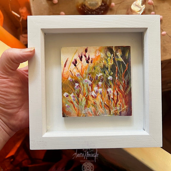miniature oil painting of wild flowers in a sunit meadow in white frame
