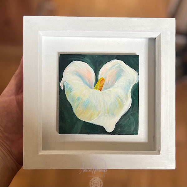 Framed artwork of a white  peace lily 
flower with a green background held by a hand.